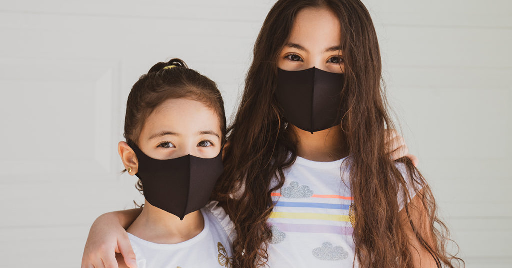 Astra Family Two girls wearing black face masks engage in a conversation, addressing children about the Corona Virus.