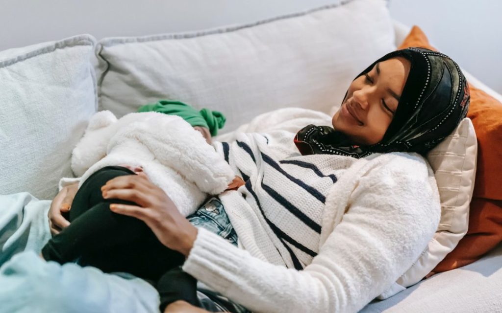 Astra Family A woman in a hijab is breastfeeding her baby on a couch while being mindful of foods to avoid when nursing.