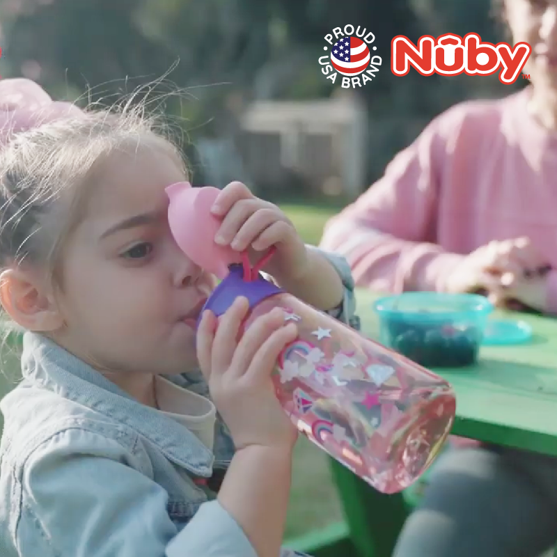 Astra Family A girl sipping from a Nuby silicone spout kids bottle at a picnic table.