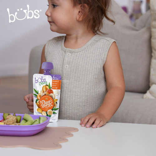 Astra Family A little girl is sitting at a table with a plate of Bubs® Organic Banana and Apricot Power Porridge, a no sugar baby food.