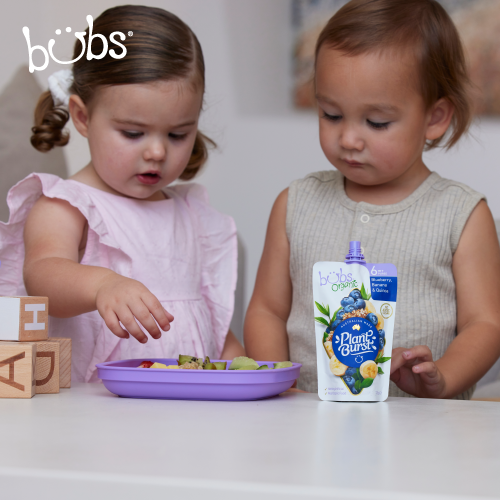 Astra Family Two little girls playing with a bowl of Bubs® Organic Blueberry, Banana and Quinoa, a healthy baby puree.