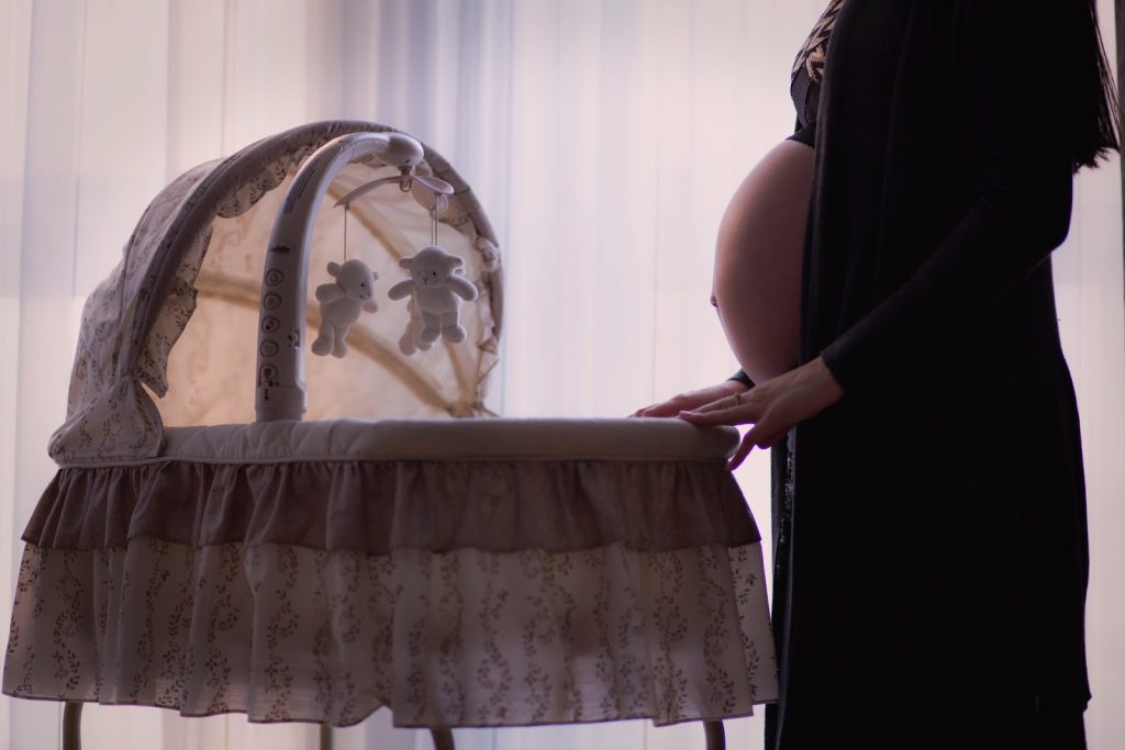 Astra Family A pregnant woman is standing next to a cradle, promoting safe sleep positions to reduce stillbirths.
