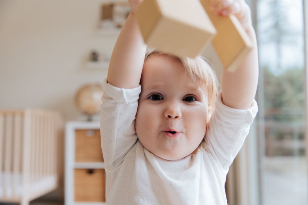 Astra Family A baby is playing with a wooden block while benefiting from prebiotic and probiotic support.