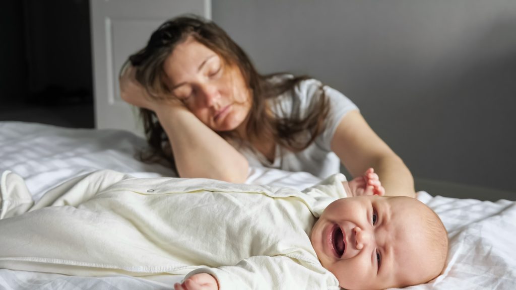 tired mother sleeps sitting floor near crying baby girl