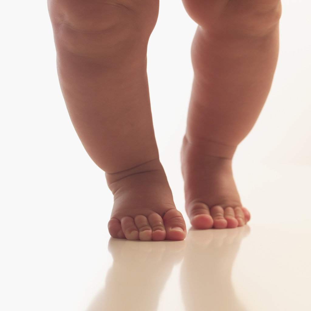 Astra Family A baby's feet are standing on a white surface. Keywords: Walking, Tiptoes